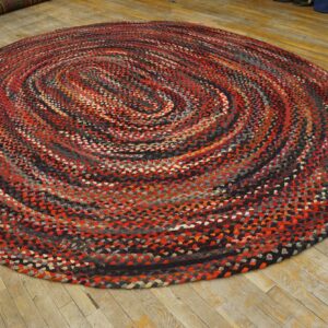 Round braided rug in red, black, and gray swirls rests on distressed wood plank flooring.