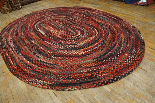 Round braided rug in red, black, and gray swirls rests on distressed wood plank flooring.