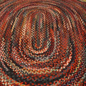 Oval braided rug with concentric red, black, and gray stripes resting on a wood floor.