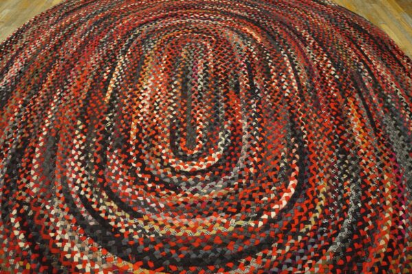 Oval braided rug with concentric red, black, and gray stripes resting on a wood floor.