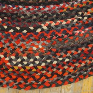 Textured, circular braided rug in black, red, and gray fabric strips with red stitching detail on wood flooring.