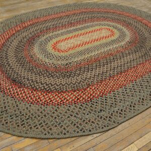 Braided oval rug featuring concentric brown, sage, and red rings rests on worn wood planks.