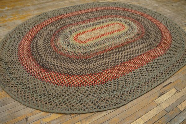 Braided oval rug featuring concentric brown, sage, and red rings rests on worn wood planks.