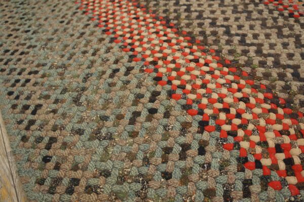 Chunky braided rug showing diagonal stripes in mixed muted teal, brown, red, and cream tones.