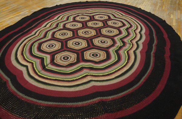 Round rug with black, burgundy, green, and tan crocheted stripes and a central hexagonal pattern.