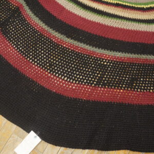 Circular rug with curved stripes of solid and mesh black, red, taupe, and green on wood flooring.