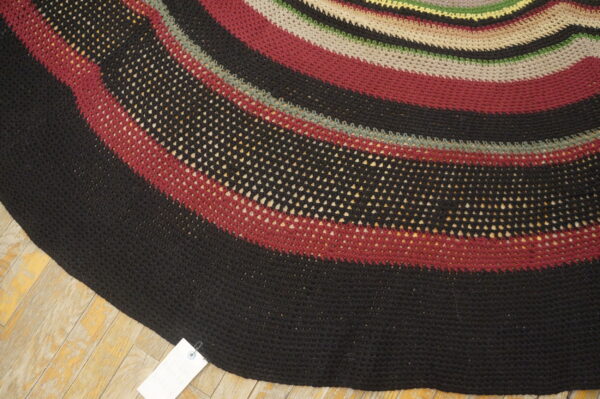 Circular rug with curved stripes of solid and mesh black, red, taupe, and green on wood flooring.