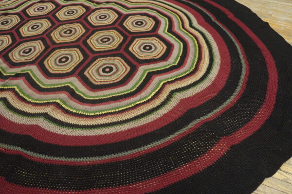 Textured round rug featuring central multicolored hexagons and wide concentric dark stripes on wood flooring.