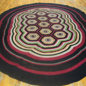 Round, multi-color textile rug with concentric wavy stripes surrounding a central pattern of linked hexagons.