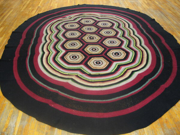 Round, multi-color textile rug with concentric wavy stripes surrounding a central pattern of linked hexagons.