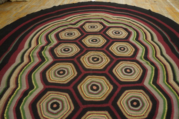 A round, multicolored crochet rug displays an all-over honeycomb pattern and striped border on wooden planks.