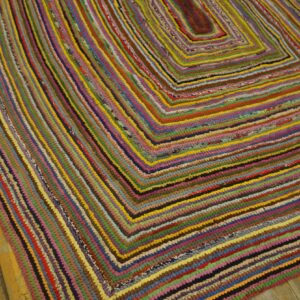 A multicolored rag rug with a concentric rectangular pattern lies on rustic wooden floorboards.