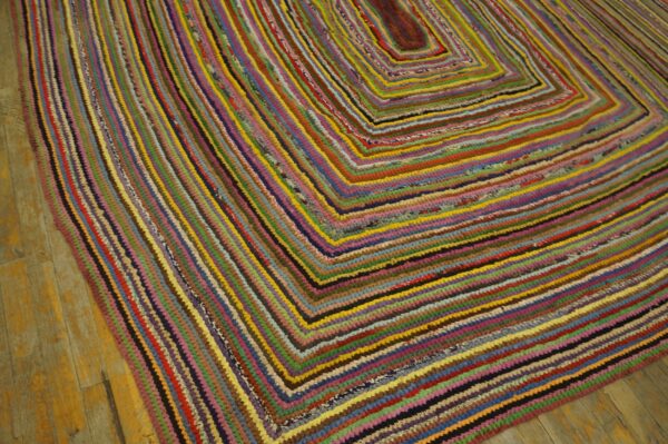 A multicolored rag rug with a concentric rectangular pattern lies on rustic wooden floorboards.