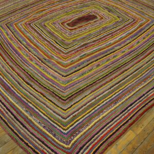 Multicolored braided rug with a concentric diamond pattern rests on golden wood plank flooring.