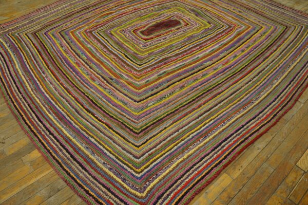 Multicolored braided rug with a concentric diamond pattern rests on golden wood plank flooring.