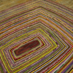 A multicolored braided rug featuring concentric rectangular stripes rests on light wood flooring.