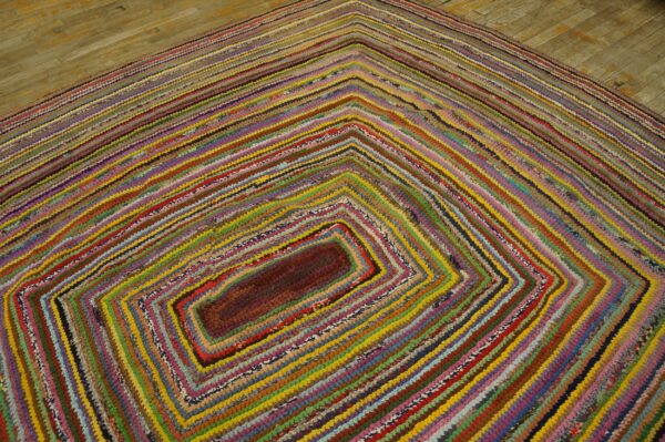A multicolored braided rug featuring concentric rectangular stripes rests on light wood flooring.