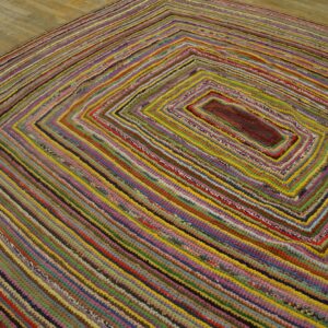 Highly textured rug features concentric multicolored braided rows on light wooden floorboards.