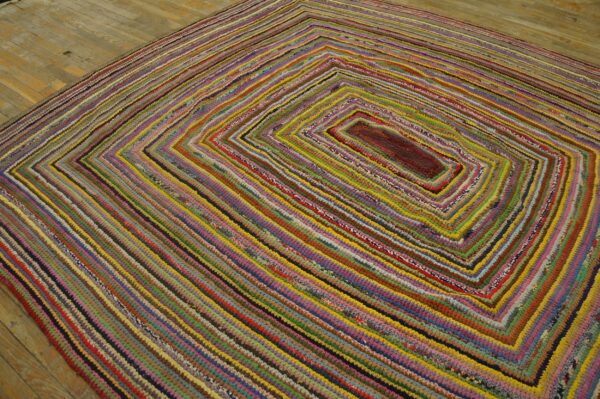 Highly textured rug features concentric multicolored braided rows on light wooden floorboards.
