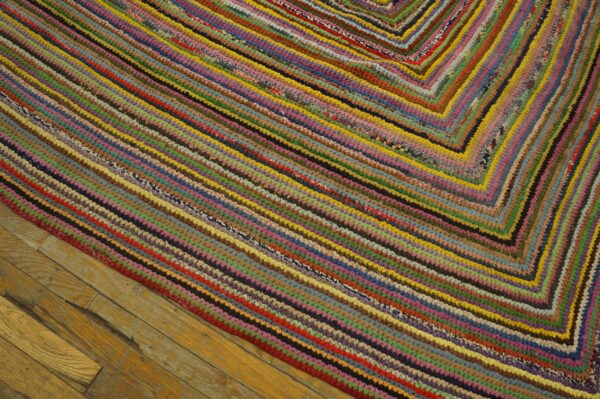 A chunky multicolored braided rug with concentric diagonal rows rests on worn wood flooring.