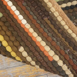 Close view of a colorful textured rug showing thick stripes of brown, yellow, orange, and green coils.