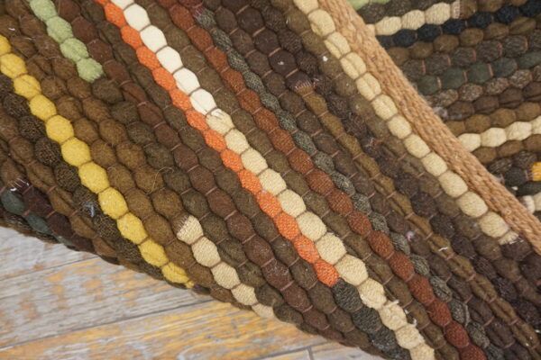 Close view of a colorful textured rug showing thick stripes of brown, yellow, orange, and green coils.