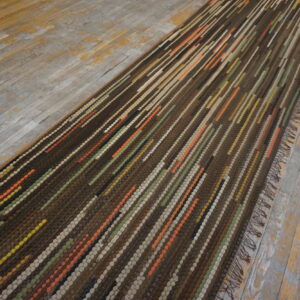 Textured brown runner with vertical stripes of orange, green, and beige on distressed plank floors.