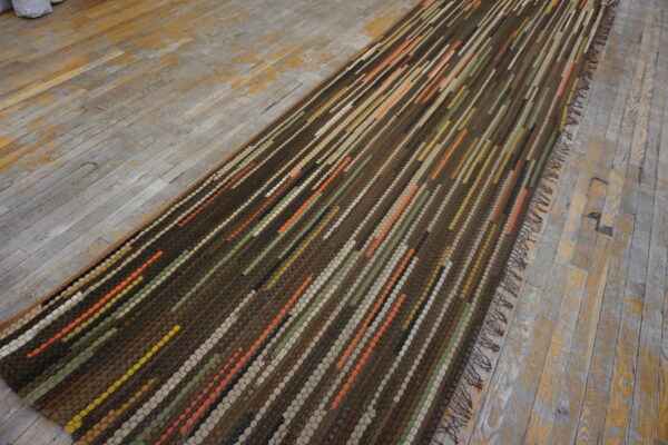 Textured brown runner with vertical stripes of orange, green, and beige on distressed plank floors.
