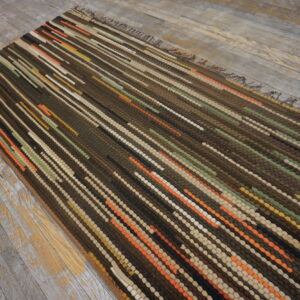 Chunky dark brown rug with textured vertical rows of orange, green, and cream on gray wood planks.