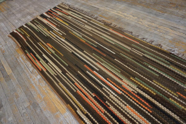 Chunky dark brown rug with textured vertical rows of orange, green, and cream on gray wood planks.