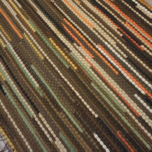 Textured striped rug in brown, orange, green, and cream sits on distressed wood floorboards.