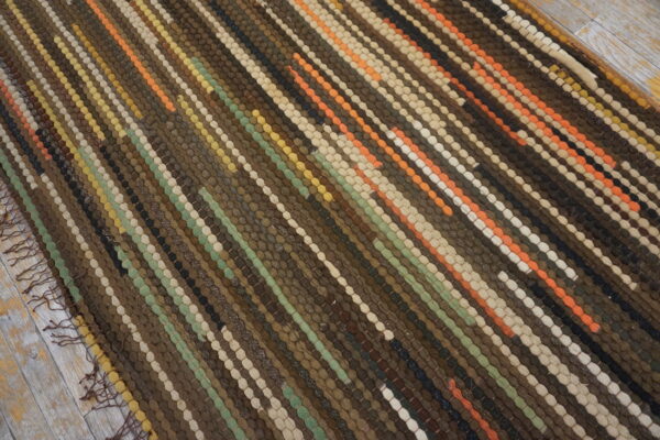 Textured striped rug in brown, orange, green, and cream sits on distressed wood floorboards.