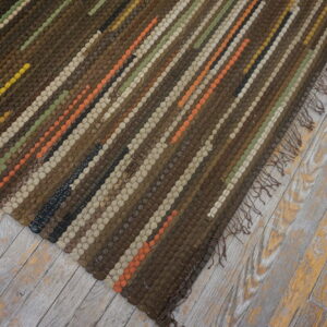 Brown woven rug with colorful stripes and fringe rests on rustic, worn wood planks.