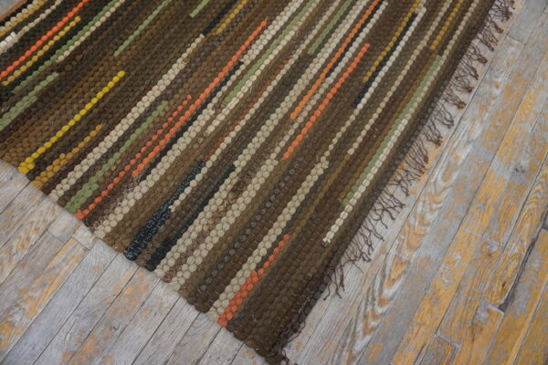 Brown woven rug with colorful stripes and fringe rests on rustic, worn wood planks.