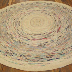 Round low-pile rug featuring multicolored flecks in concentric rings on a cream background over wood planks.