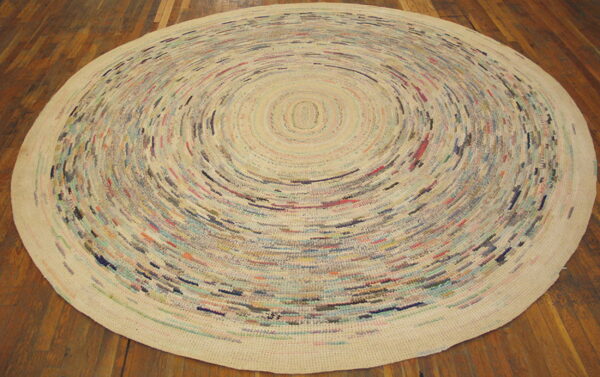 Round low-pile rug featuring multicolored flecks in concentric rings on a cream background over wood planks.