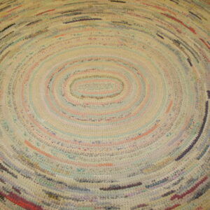 Close-up of a braided rag rug with concentric oval bands in mixed pastel colors and cream.