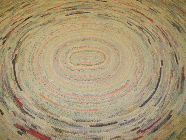 Close-up of a braided rag rug with concentric oval bands in mixed pastel colors and cream.