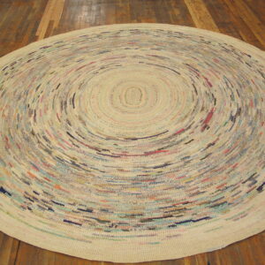 Round cream rag rug featuring colorful flecks in a tight concentric spiral pattern rests on dark wood planks.