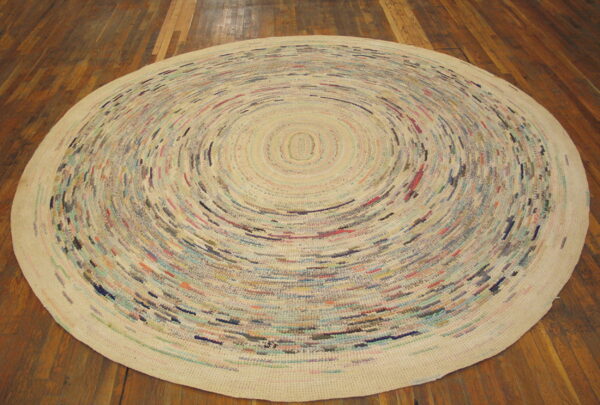 Round cream rag rug featuring colorful flecks in a tight concentric spiral pattern rests on dark wood planks.