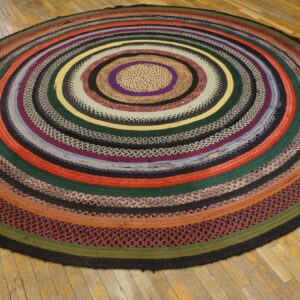Round braided rag rug displaying many colorful concentric rings sits on pale yellow wood planks.