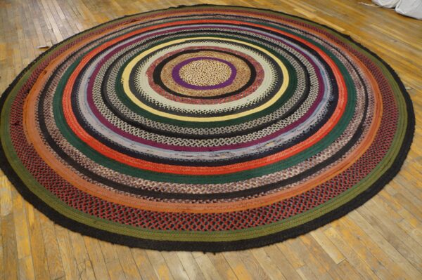 Round braided rag rug displaying many colorful concentric rings sits on pale yellow wood planks.