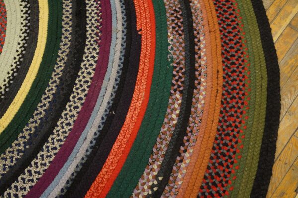 Close-up of a circular, thick braided rug with many concentric multicolored bands on hardwood floor.