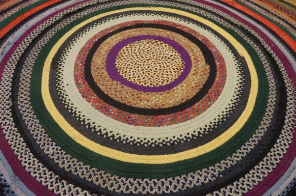 Multicolor braided round rug with concentric circles of tan, purple, yellow, green, cream, and patterned bands.