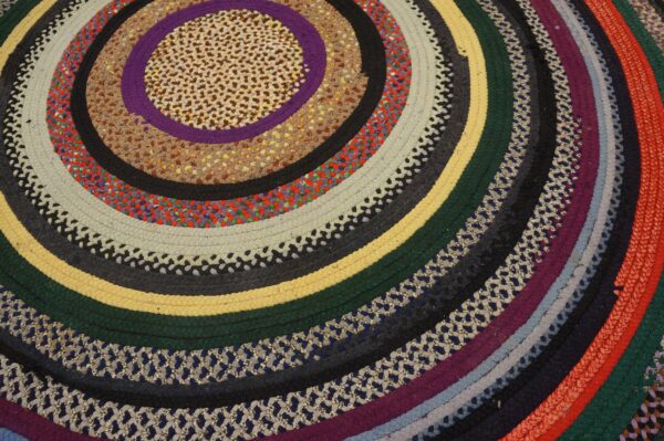 Colorful braided circular rug with rings of multicolored, textured stripes in varying widths.