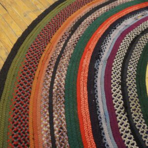 Multicolor braided rug with curved stripes and patterned bands lies on distressed wooden floor.
