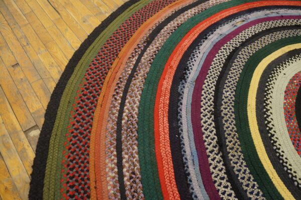 Multicolor braided rug with curved stripes and patterned bands lies on distressed wooden floor.