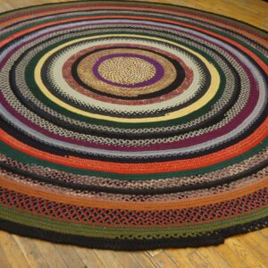 Circular braided rug with concentric stripes in red, green, purple, yellow, and black on hardwood floors.