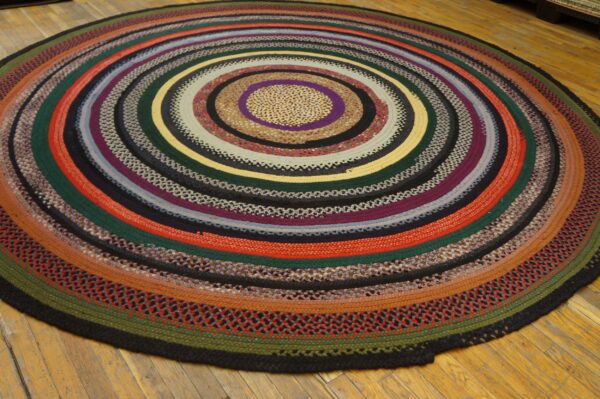 Circular braided rug with concentric stripes in red, green, purple, yellow, and black on hardwood floors.