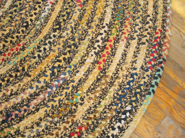 Braided area rug, speckled cream and black with colorful accents, rests on diagonal hardwood flooring.